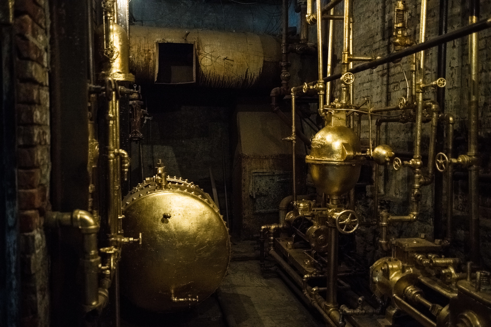 Photograph of a dingy boiler room where metal pipes are adorned with tiny knobs